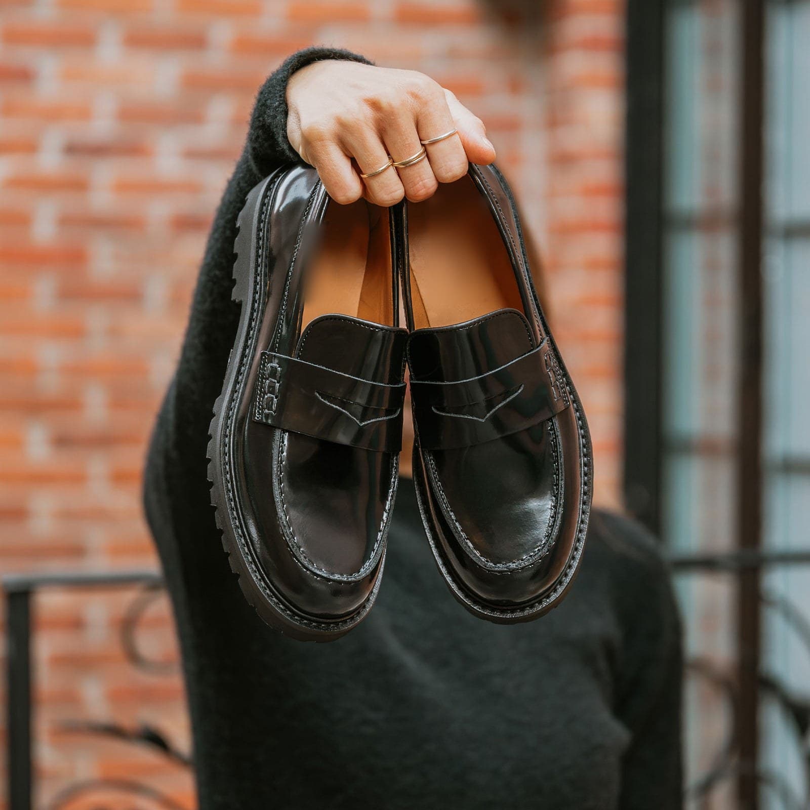Black penny loafers held in one hand